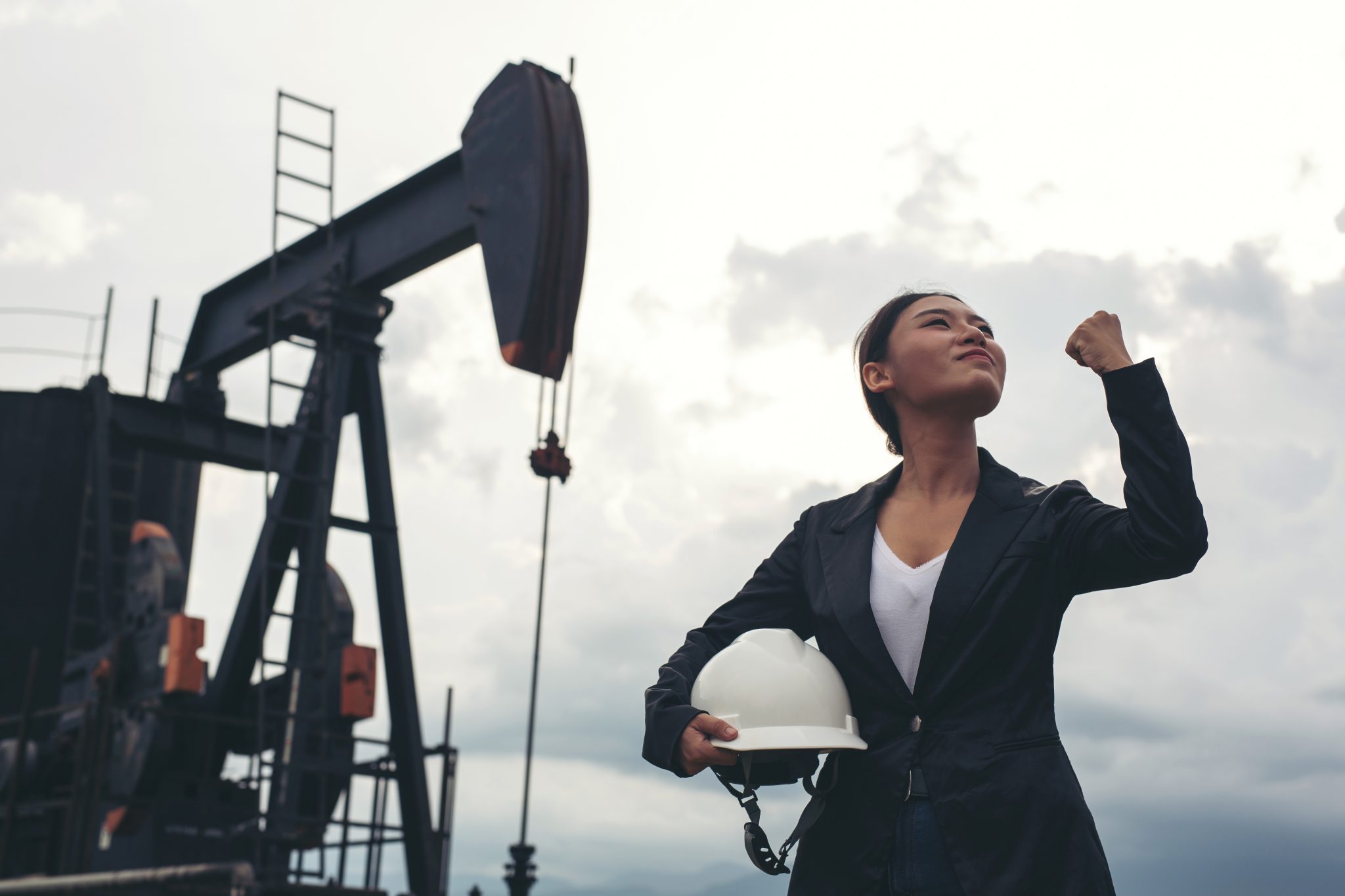 Notre ambition female engineer standing with working oil pumps with a white sky